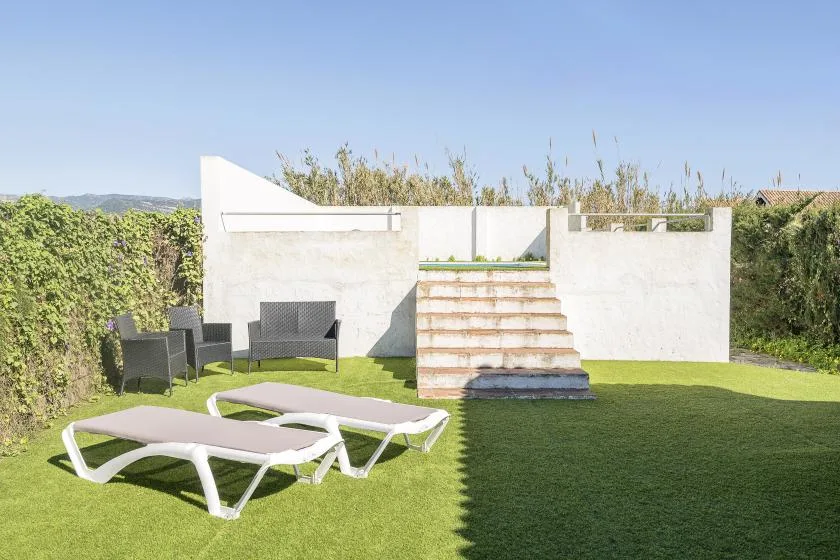 An outdoor patio with lounge seating, green lawn, and steps leading to a raised area.