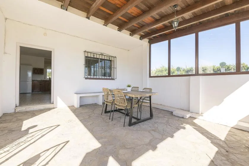 A covered patio with a dining table and large windows.
