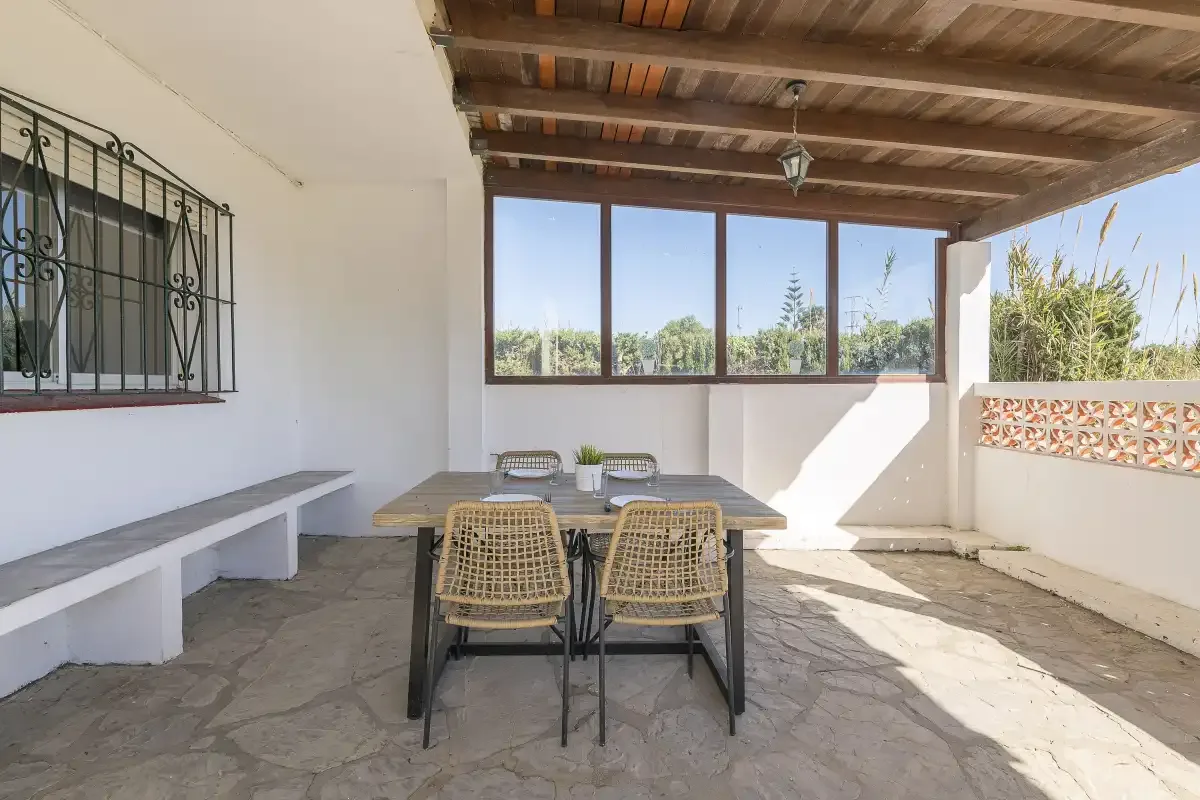 A covered outdoor dining area with a table and woven seating.
