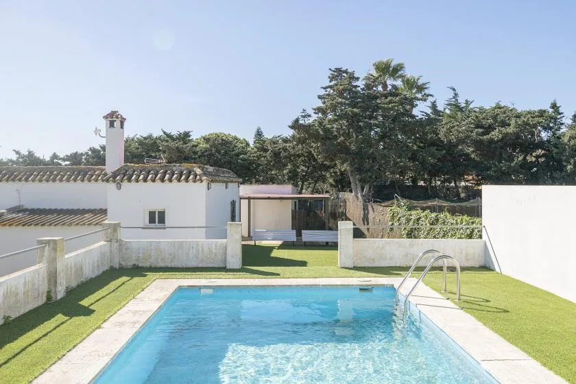 An outdoor swimming pool sits beside a low white building and a grassy yard.