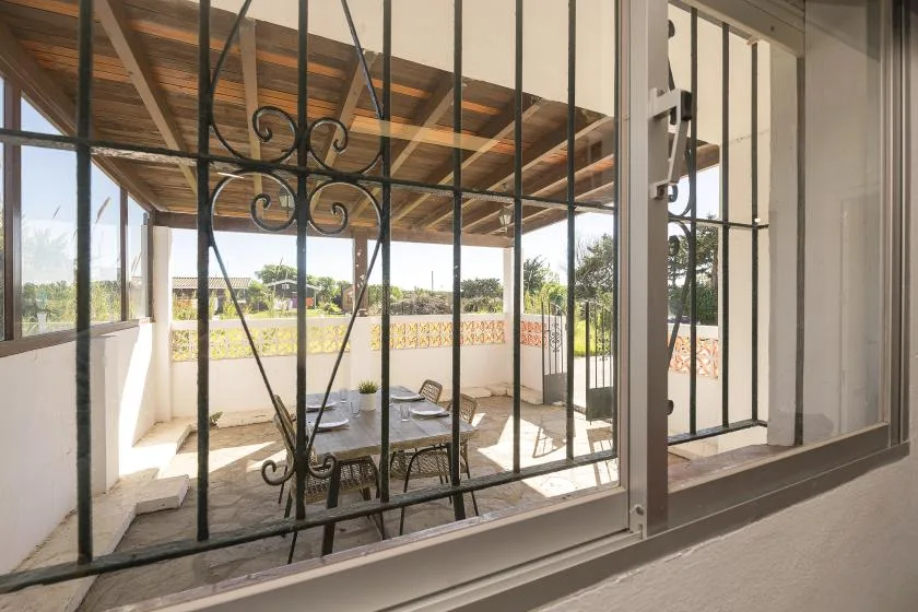 A covered outdoor patio with a table and seating is seen through a barred window.