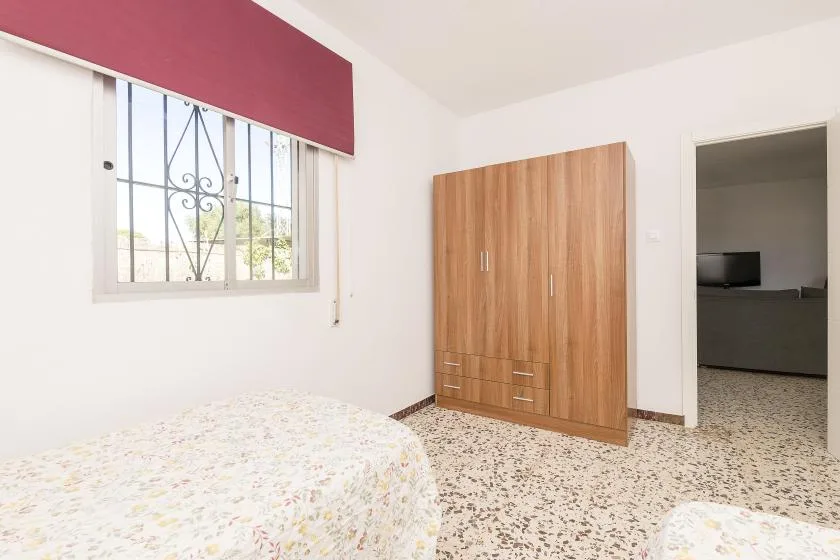 A bedroom with a bed, wooden wardrobe, and barred window.