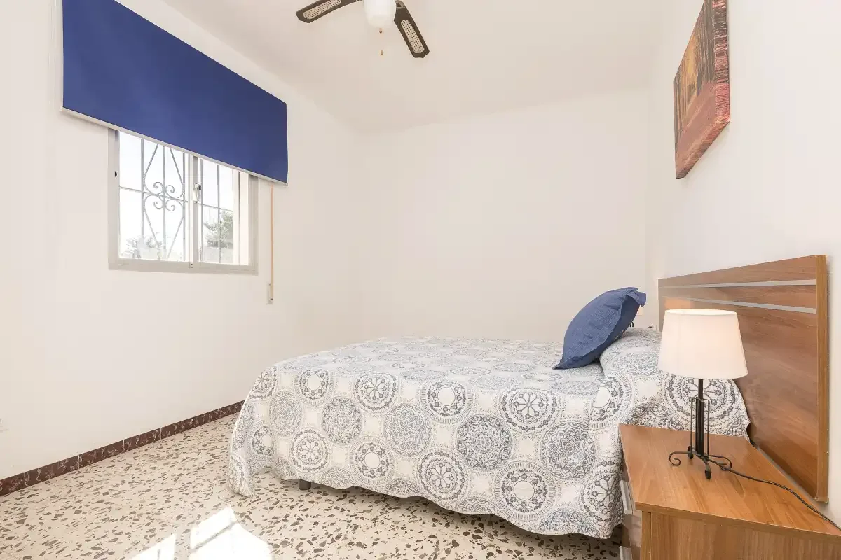 A bedroom with a patterned bedspread and a window with a blue shade.