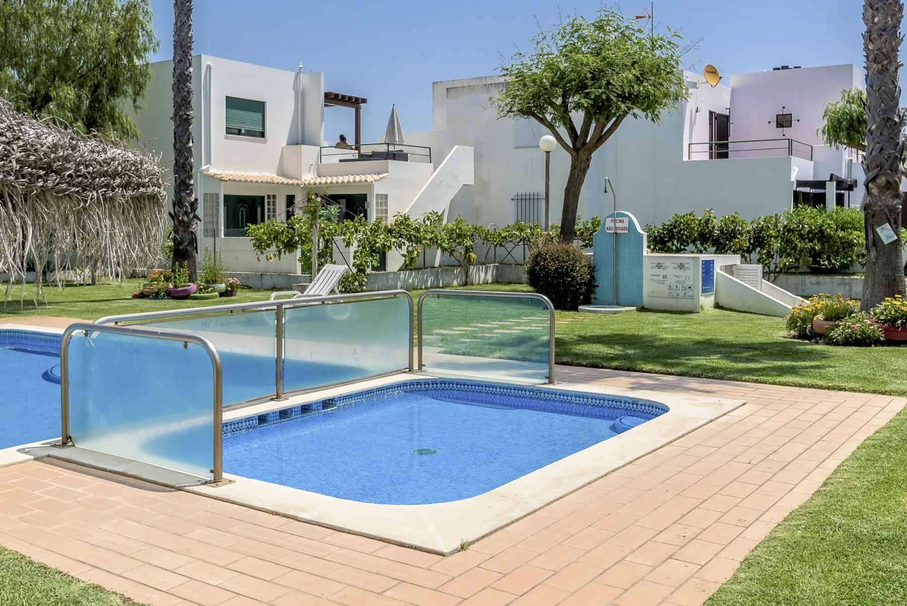 An outdoor swimming pool sits beside a paved patio and landscaped garden.