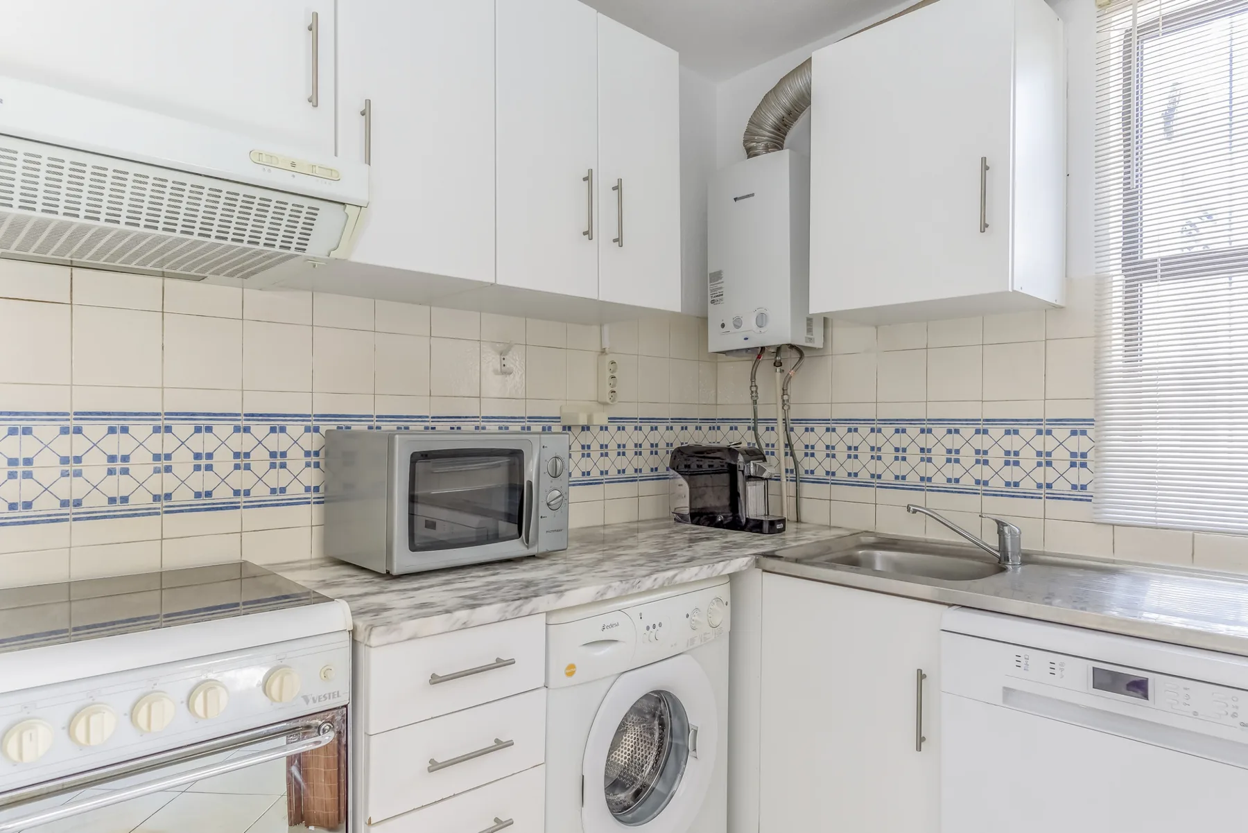 A compact kitchen with white cabinets, a microwave, and a washing machine.