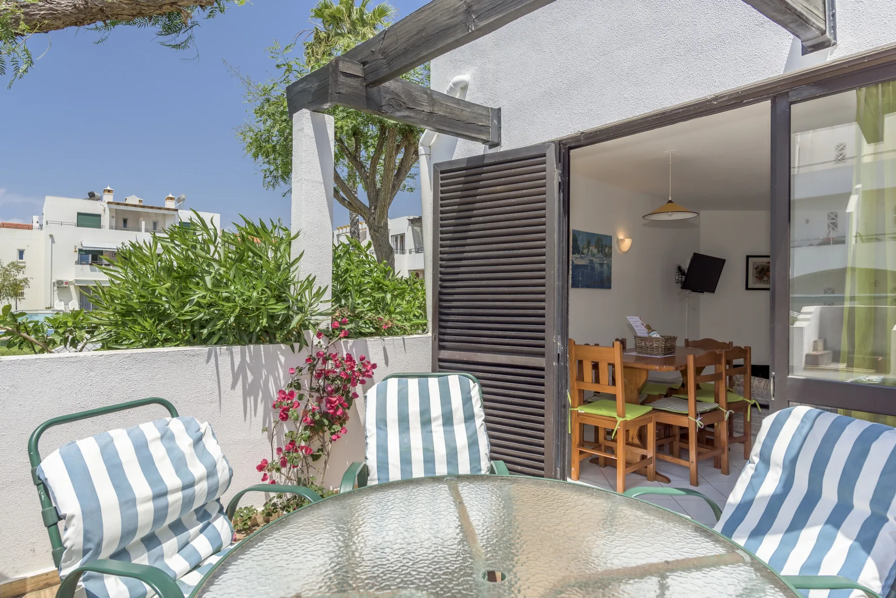 A patio seating area with a glass-top table overlooks a dining area through open doors.