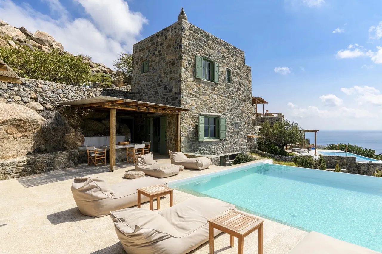 A stone villa patio with a swimming pool and cushioned seating.