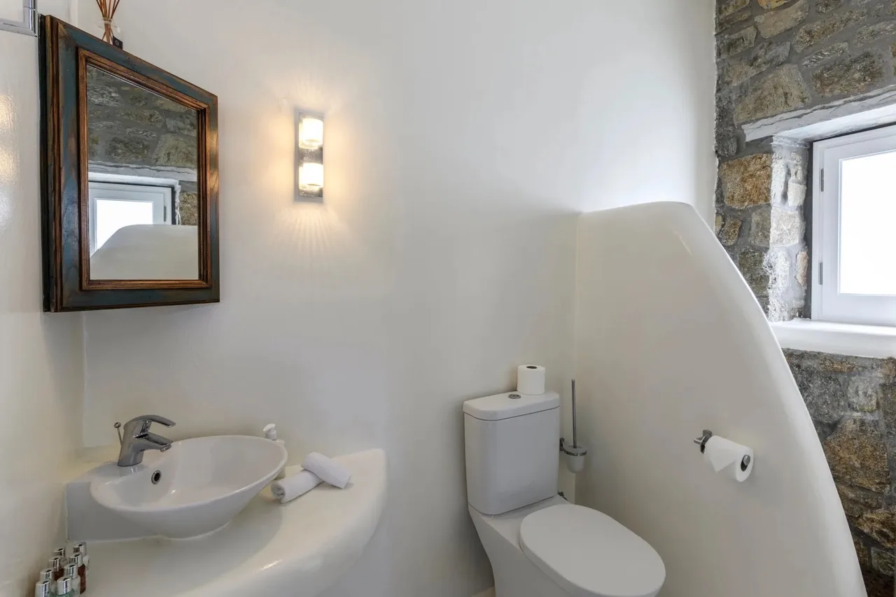 A bathroom with a sink, toilet, and stone-framed window.