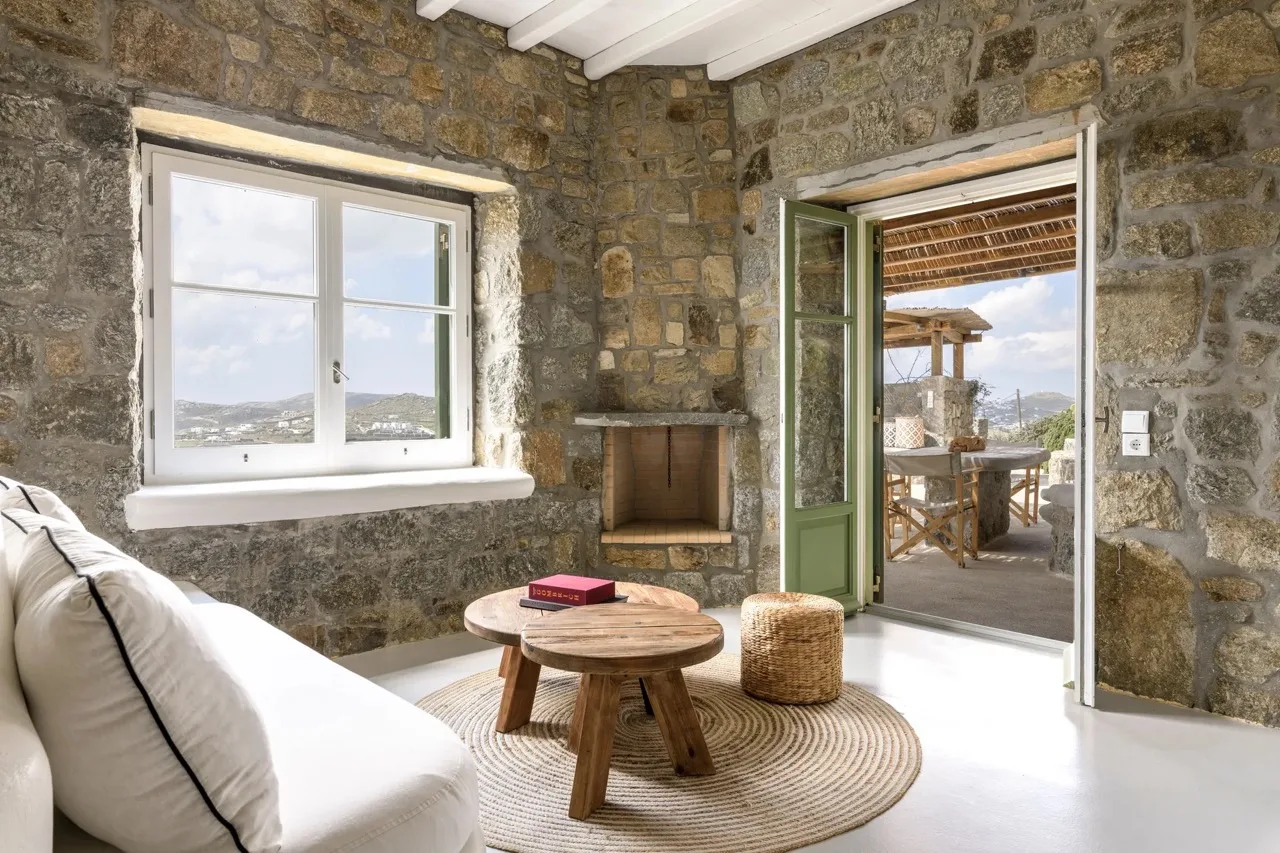 A stone-walled living room opens onto a sunlit outdoor seating area.