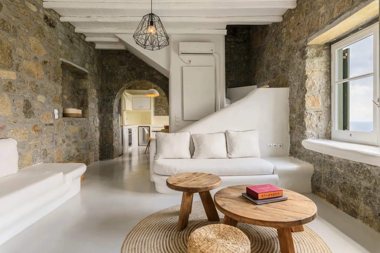 A stone-walled living room with white seating and round wooden tables.