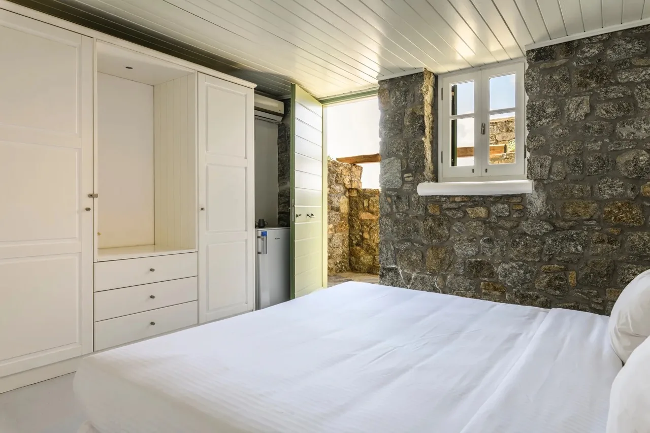 A bedroom with a white bed, built-in wardrobes, and stone walls.