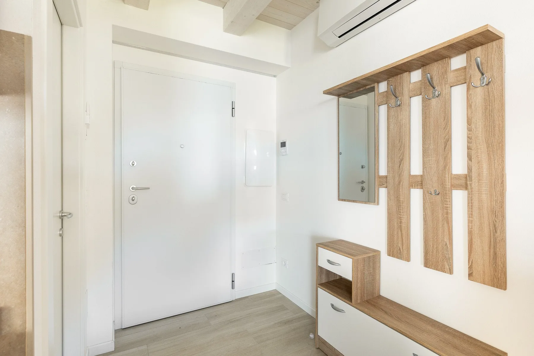 Una entrada luminosa con una puerta blanca, ganchos de pared y un banco estrecho.