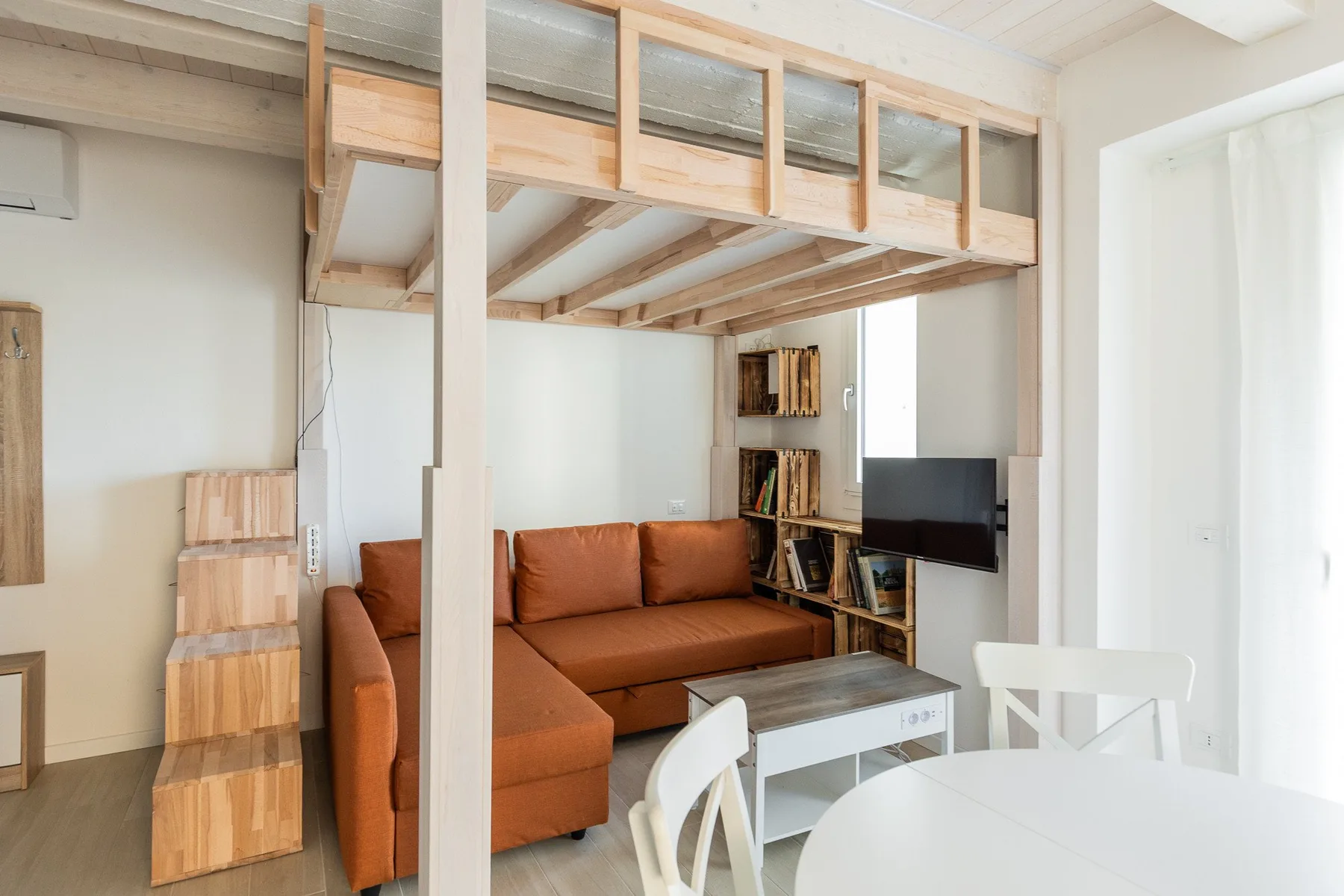 Una luminosa sala de estar con un sofá seccional marrón bajo una cama alta de madera.