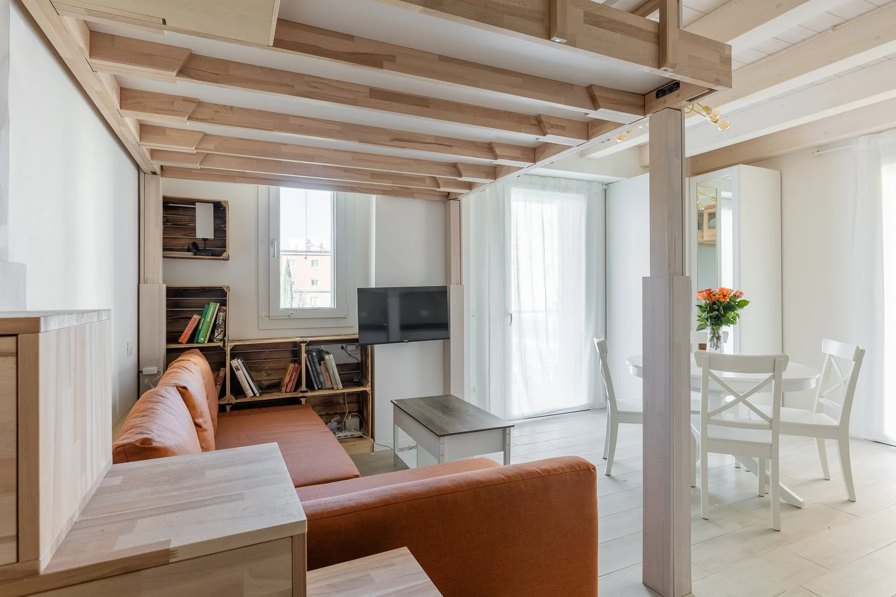 Una luminosa sala de estar y comedor con asientos, un televisor y una mesa junto a las ventanas.
