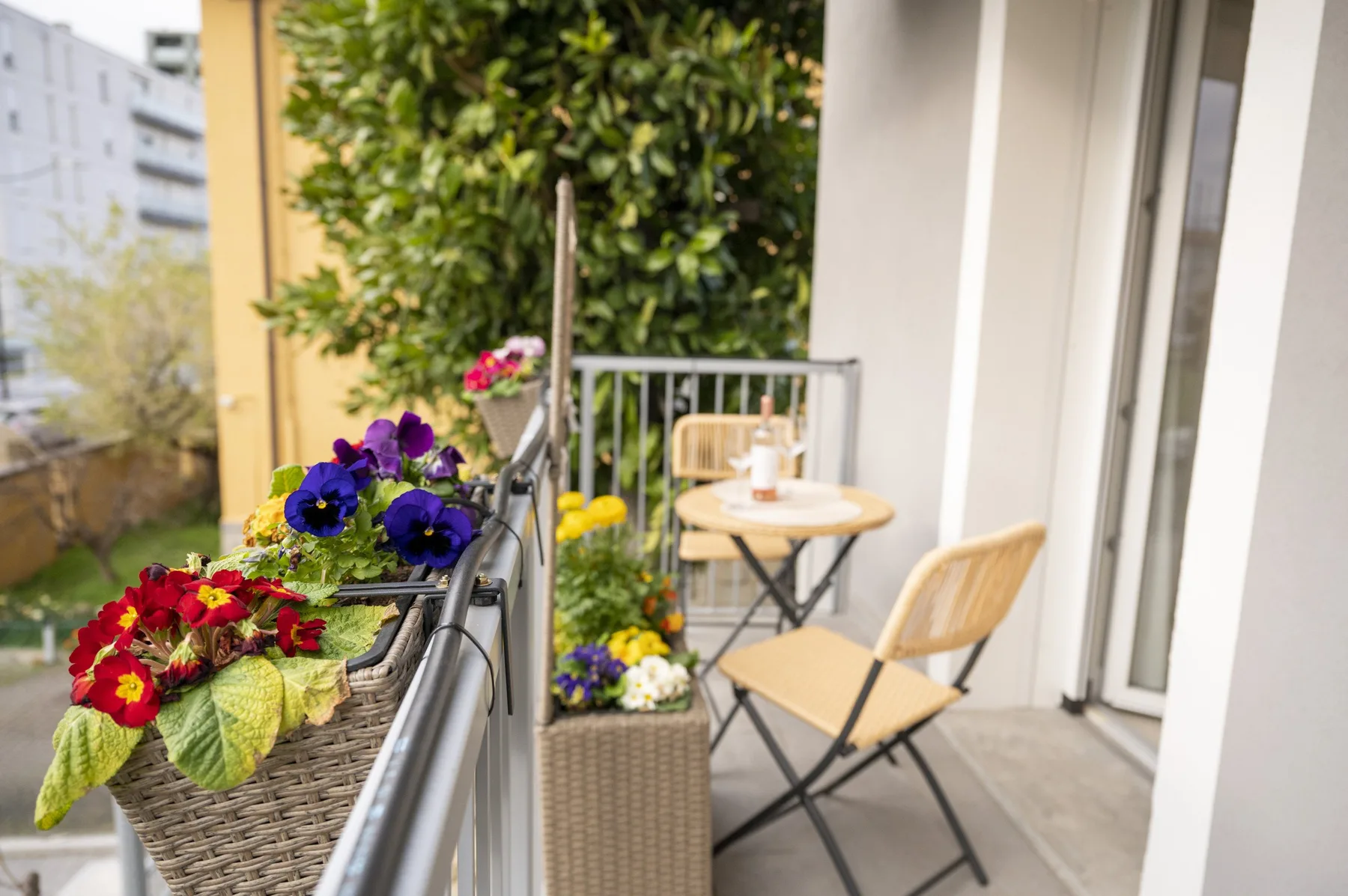 Un espacio de estar en un balcón con una mesa pequeña y flores en macetas.