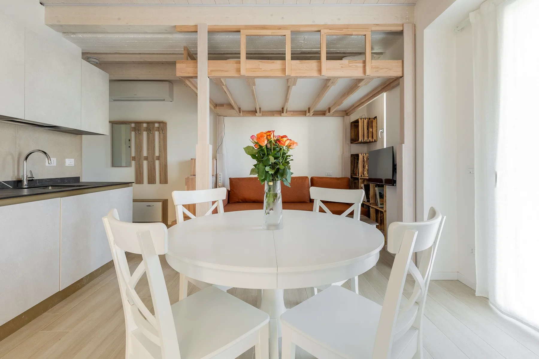 Un comedor luminoso con una mesa redonda y flores junto a una cocina abierta.