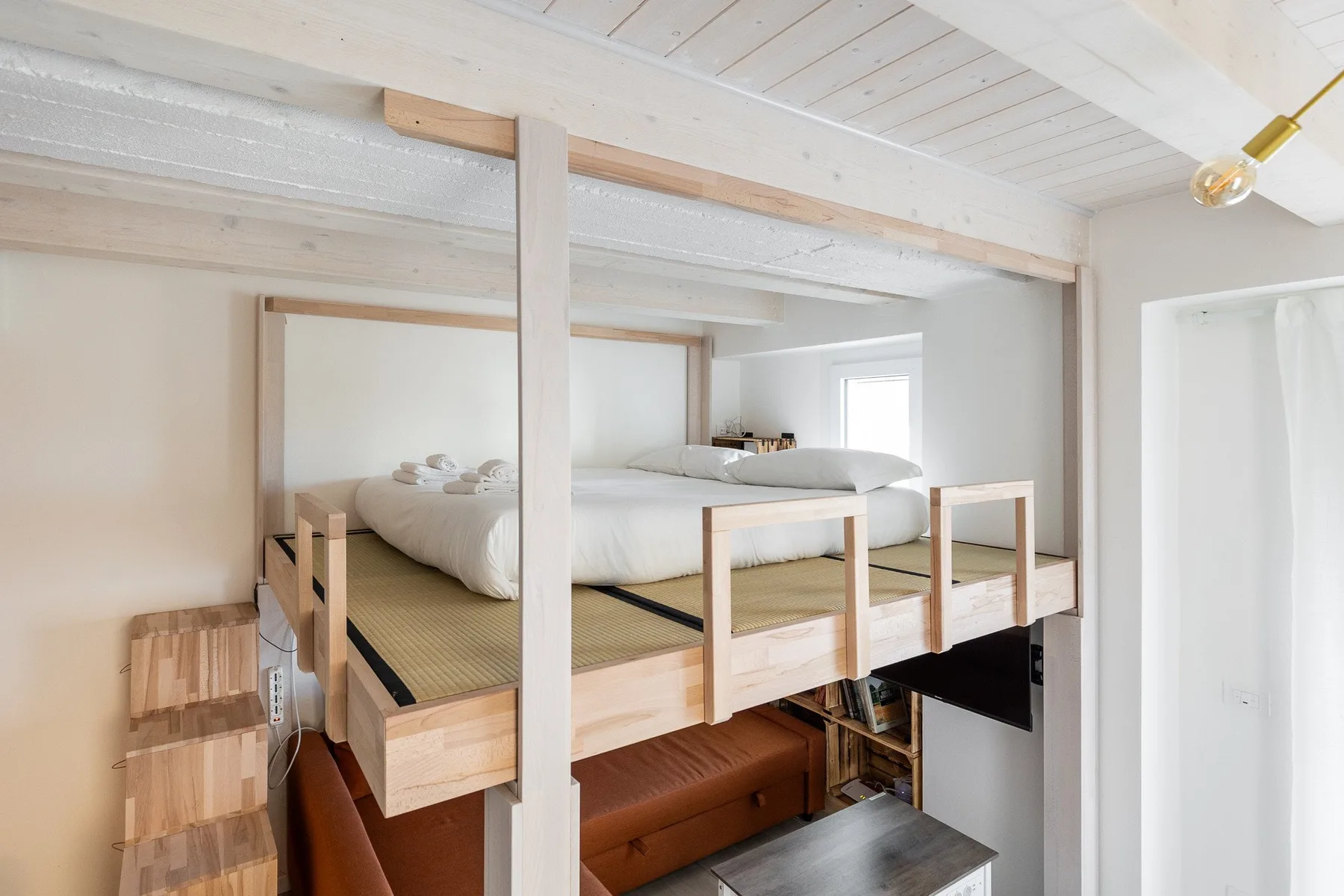 Una zona elevada para dormir con una cama y barandilla de madera sobre una zona de estar.
