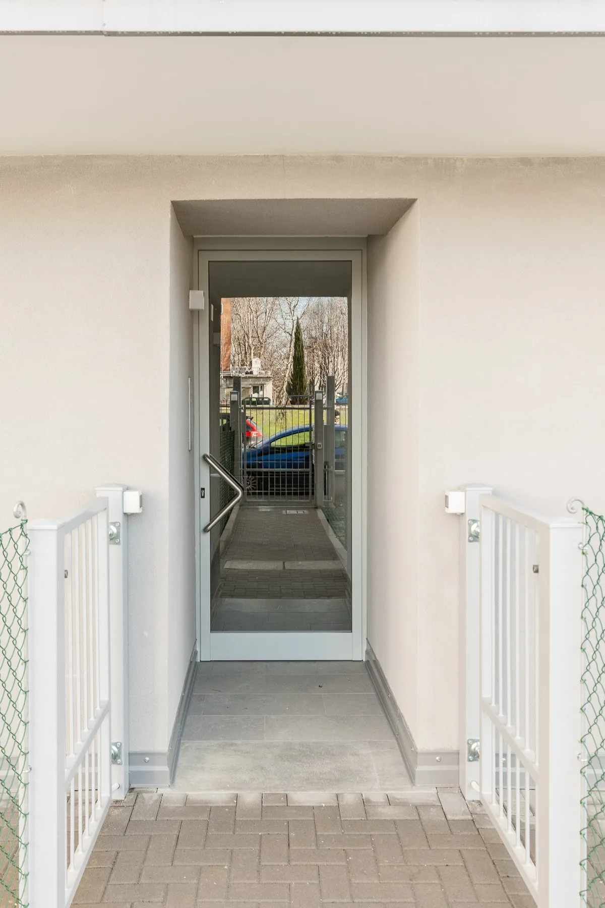 Un pasaje de entrada cubierto conduce a una puerta de vidrio, con barandillas a ambos lados.