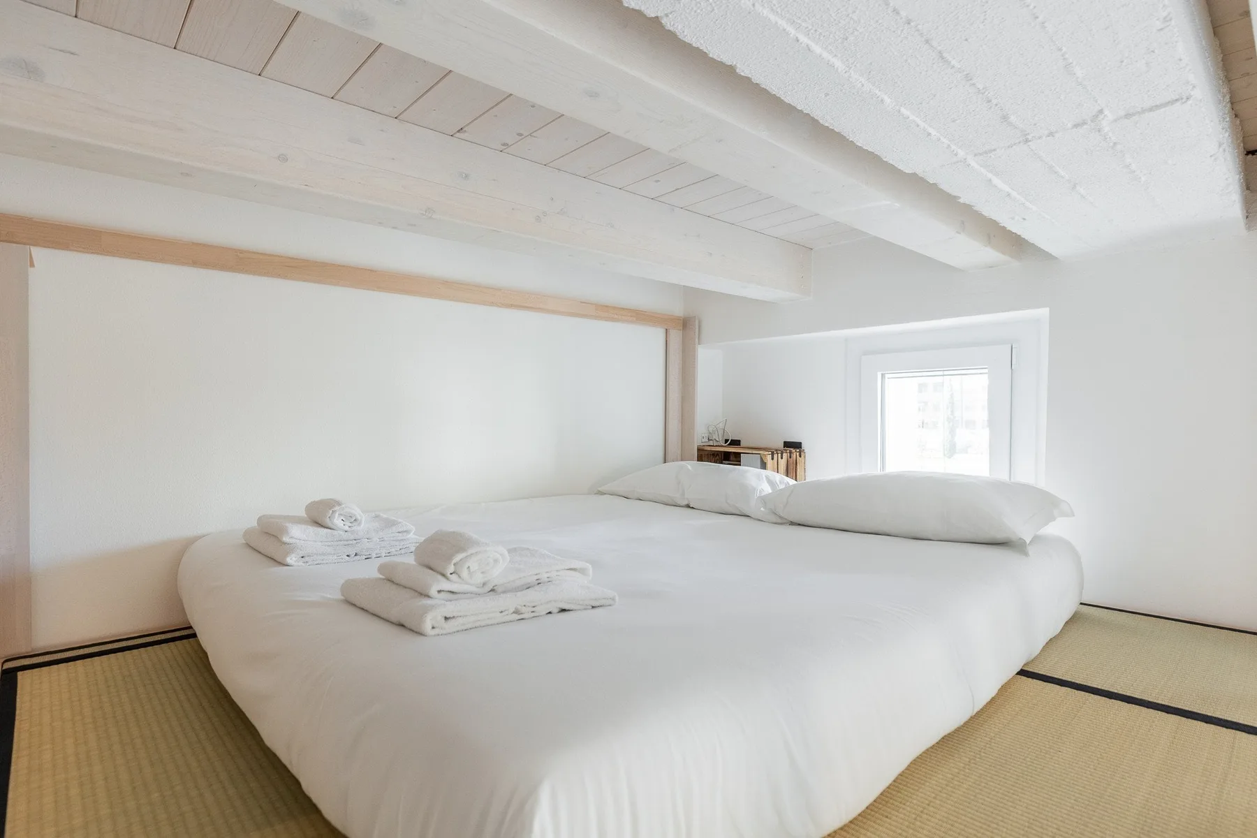 Un dormitorio luminoso con una cama baja vestida con ropa de cama blanca.