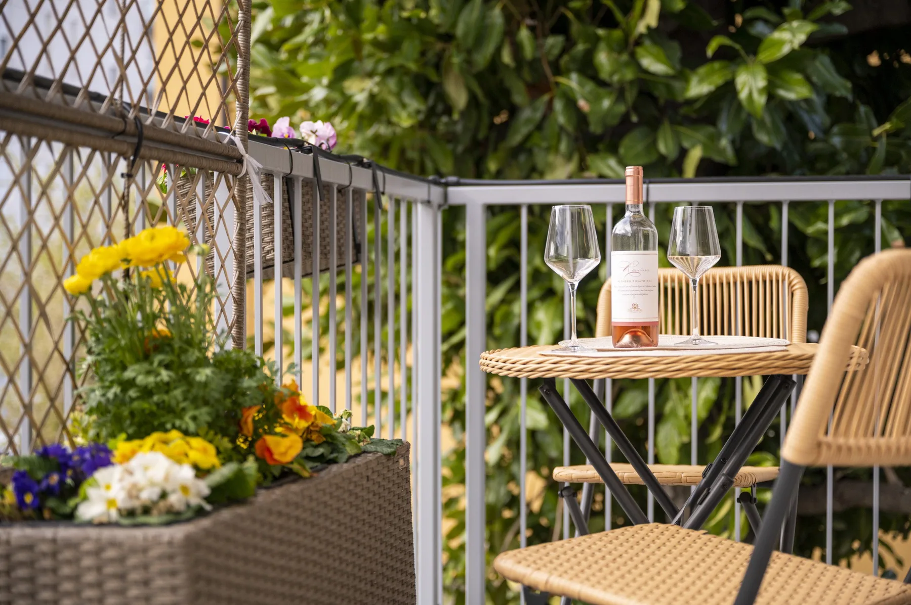 Un pequeño patio al aire libre con una mesa, sillas, copas de vino y flores en macetas.
