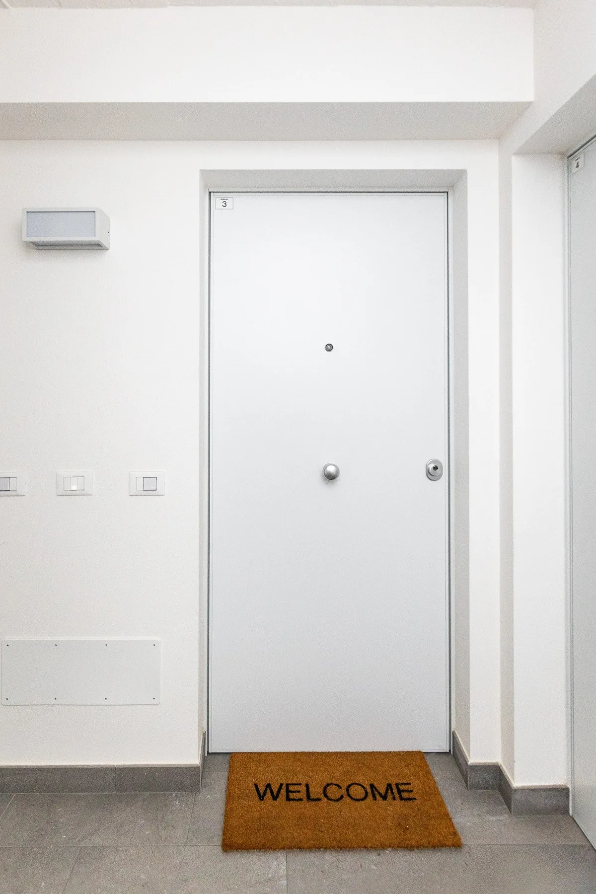 Una puerta blanca da a un pasillo con un felpudo de bienvenida.