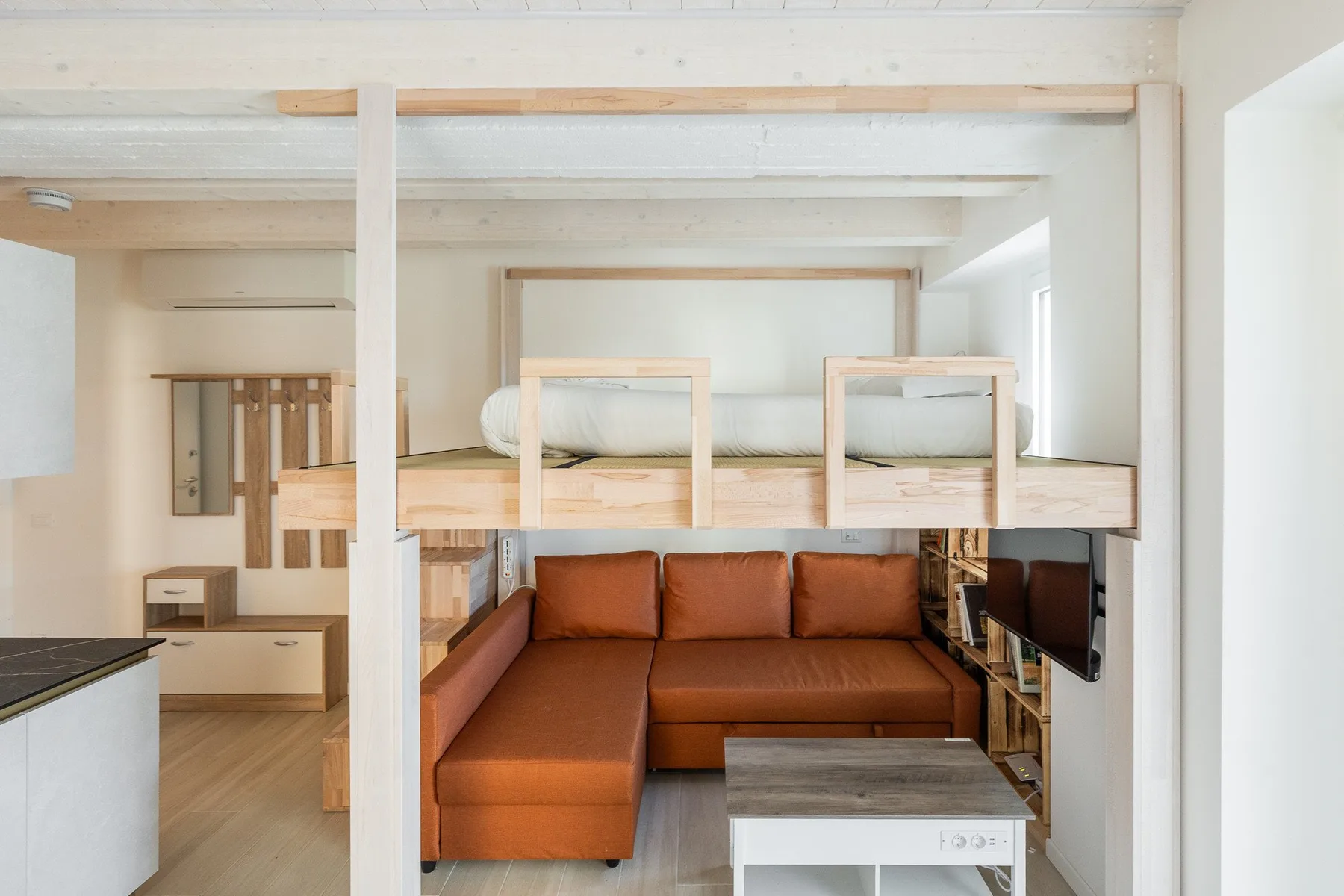 Un dormitorio compacto con una cama elevada sobre una zona de asientos marrones.