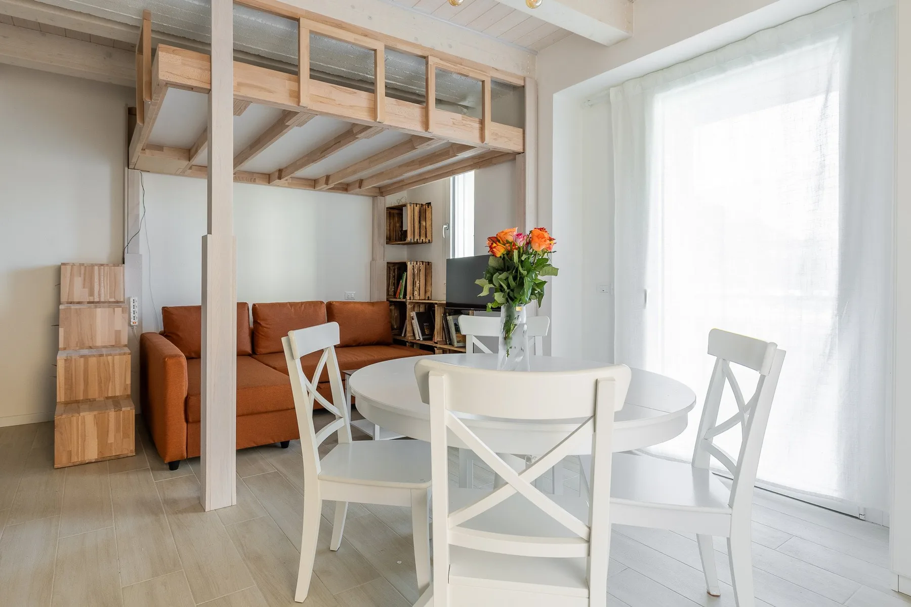 Un comedor luminoso con una mesa redonda y sillas blancas junto a una zona de estar.