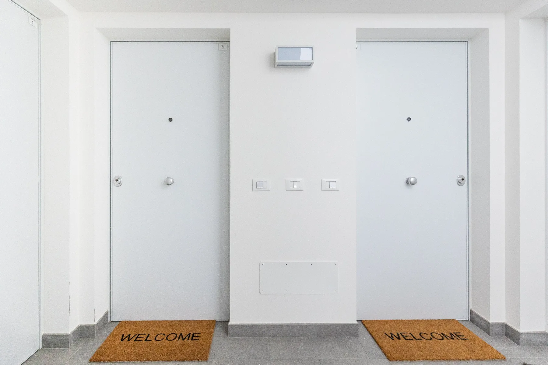 Una entrada interior con dos puertas blancas y felpudos de bienvenida.
