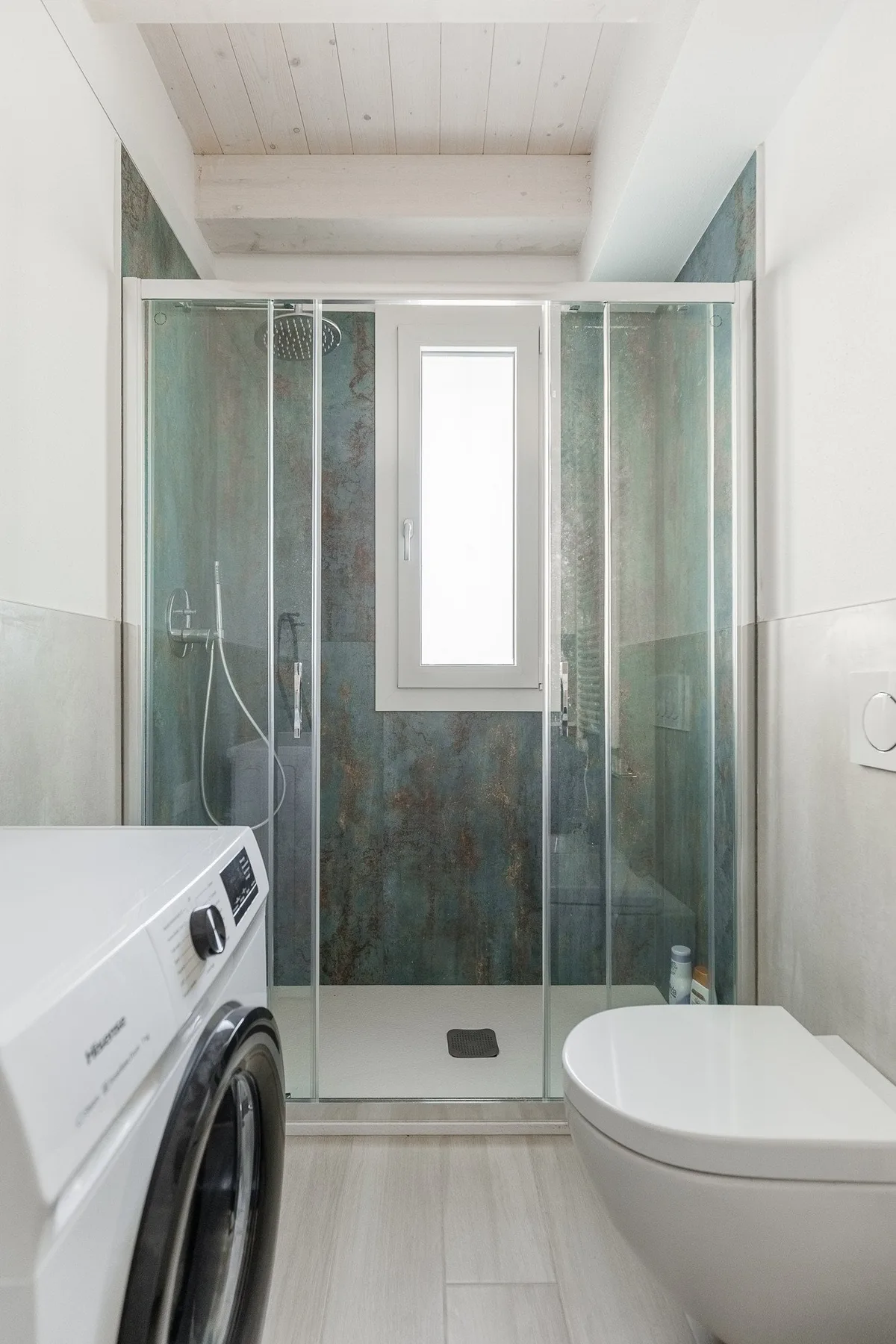 Un baño compacto con ducha de vidrio, inodoro y lavadora.