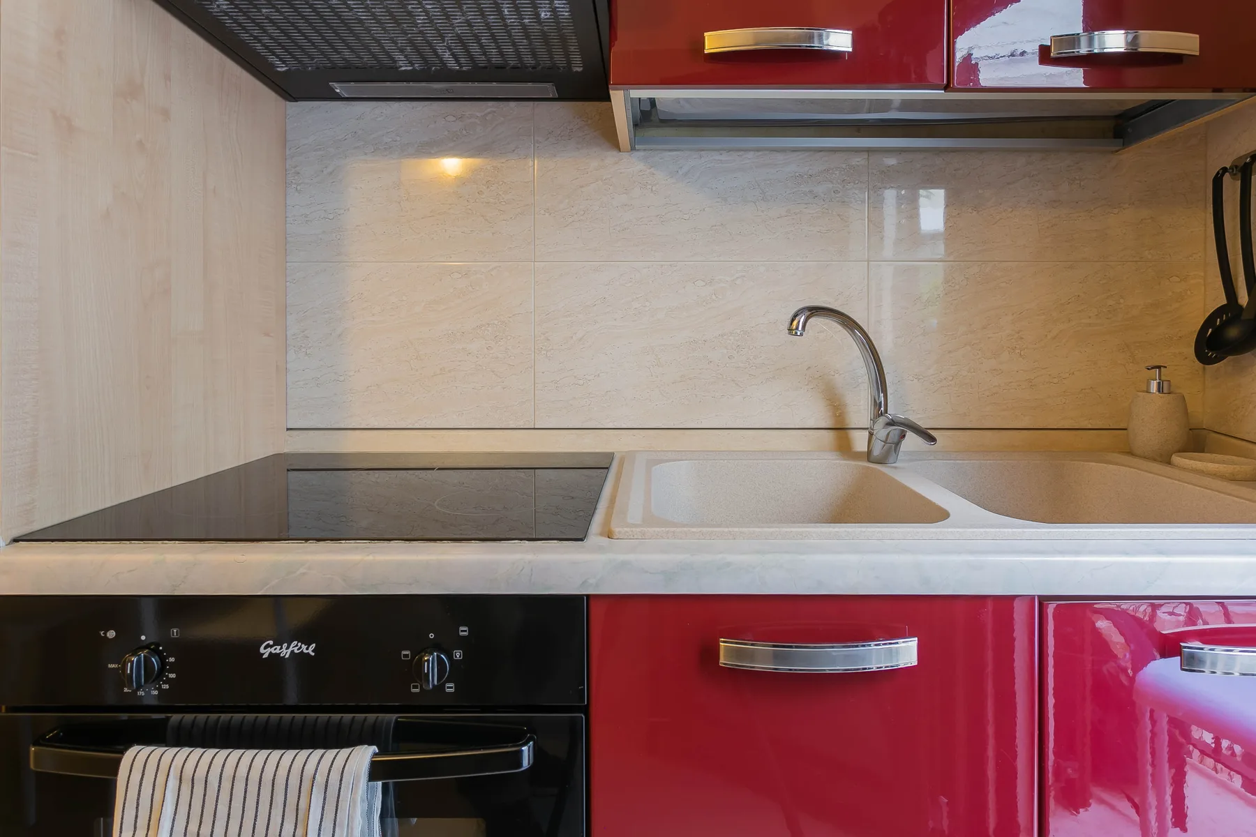 A compact kitchen with a cooktop, sink, and red cabinets.