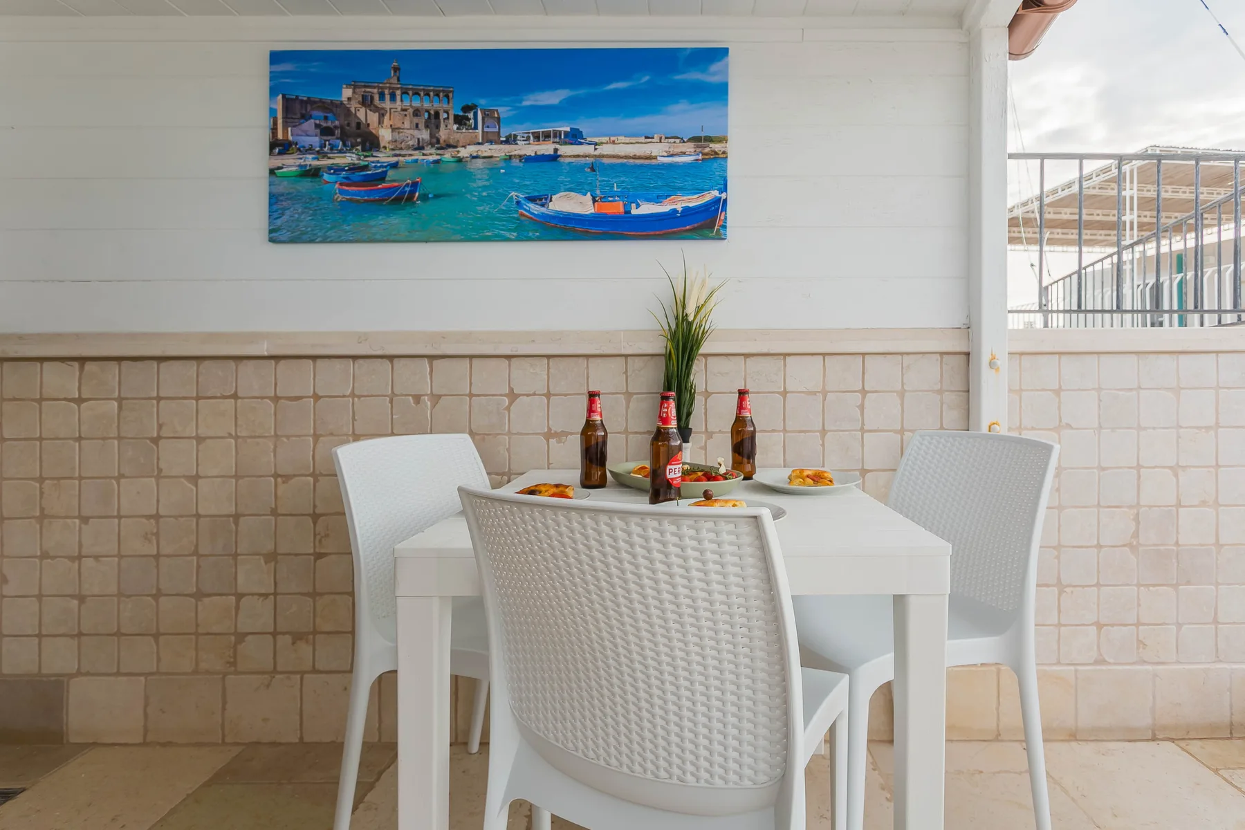 A dining area with a white table and chairs beneath a colorful harbor picture.