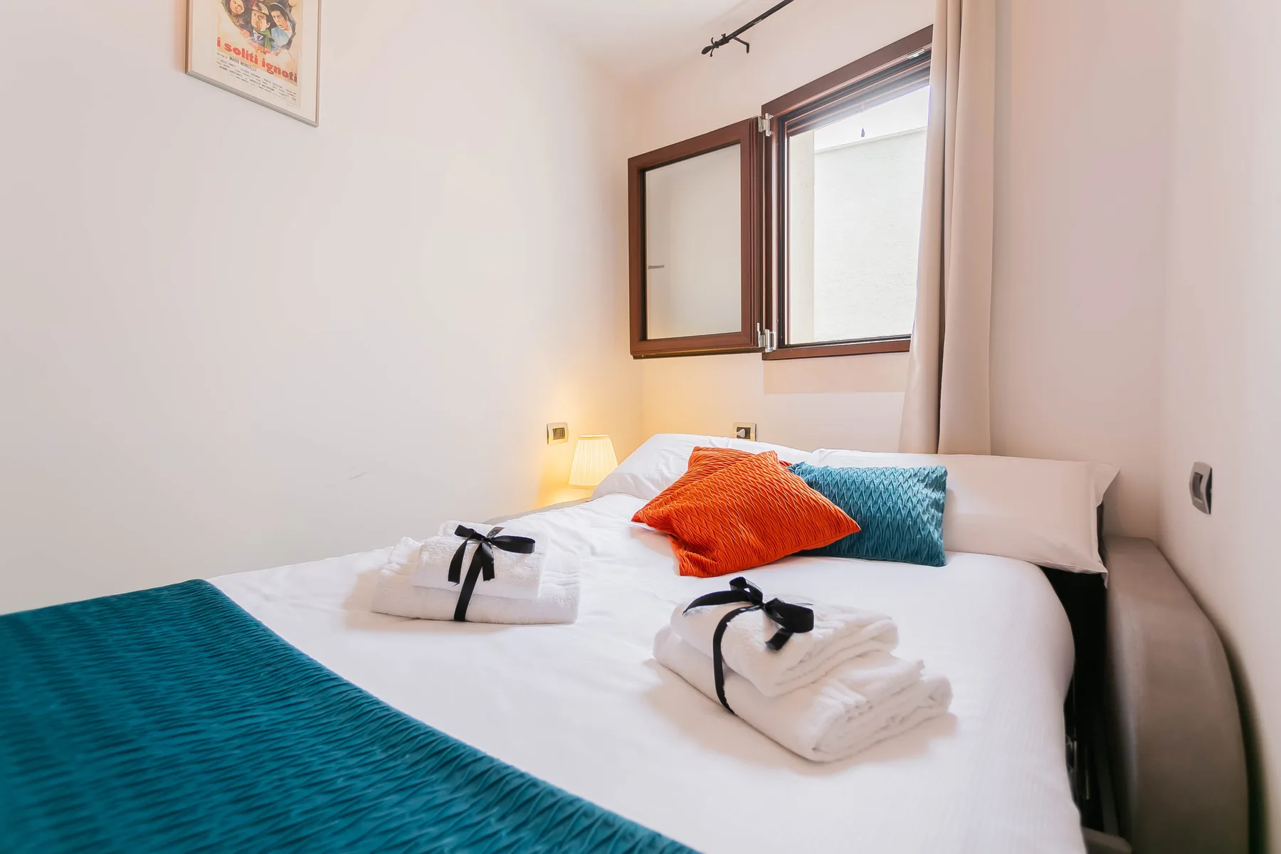 A bedroom with white bedding, colorful cushions, and a window.