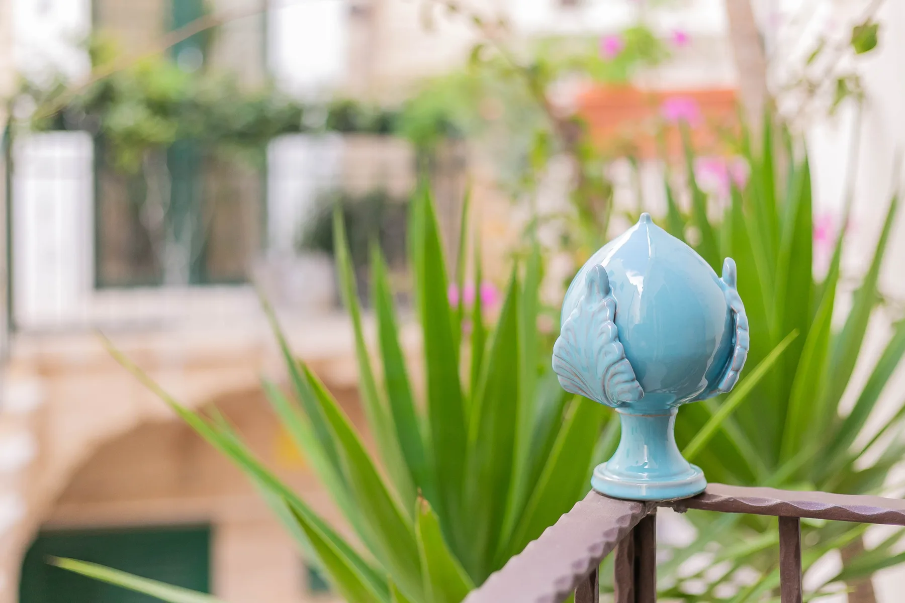 A blue decorative finial sits beside tall green plants on a railing.