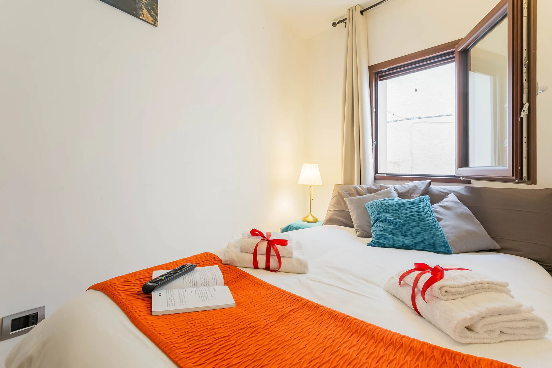 A bedroom with a neatly made bed and a window beside it.