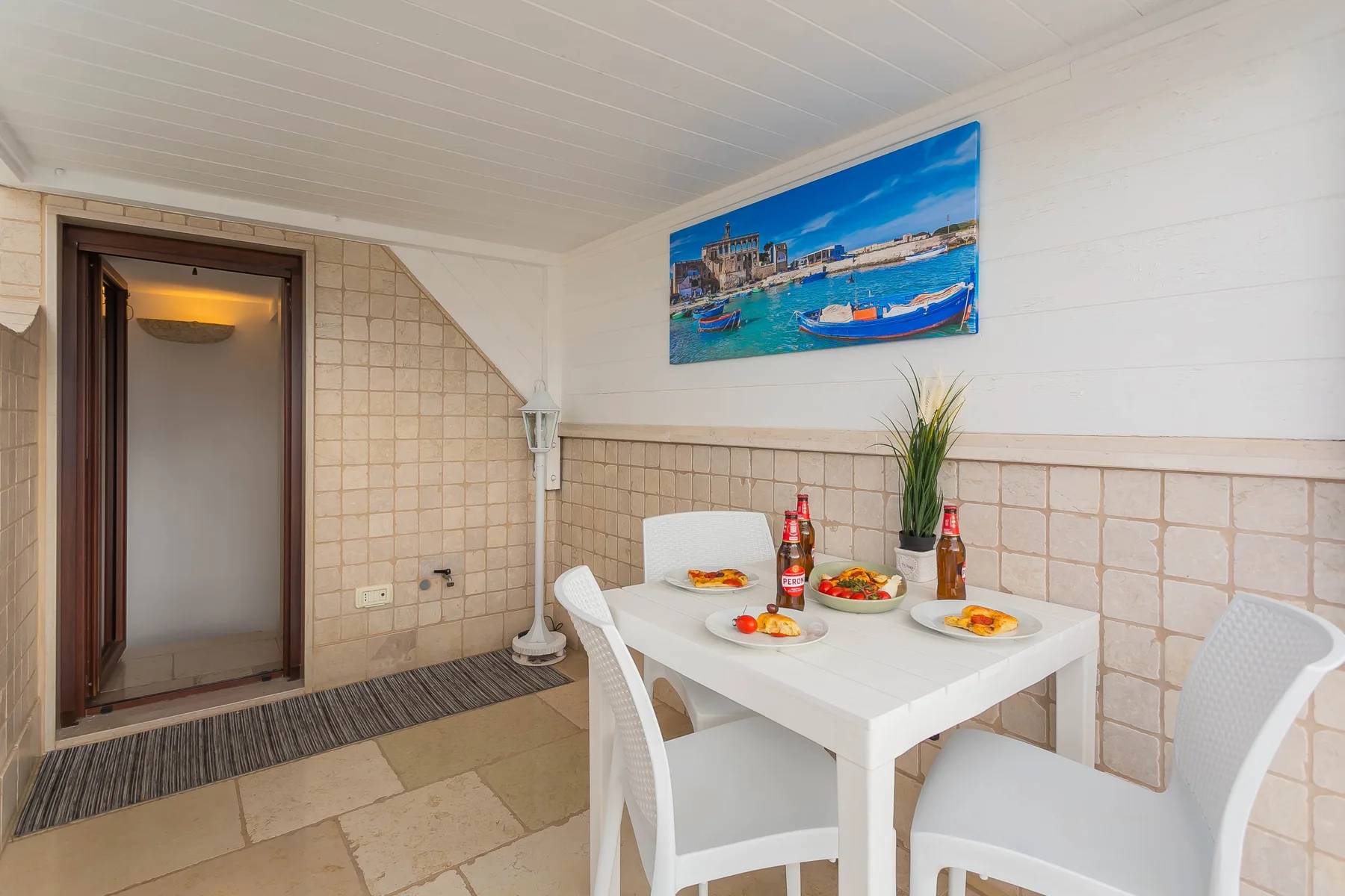 A tiled dining area has a white table set with plates beneath a colorful wall picture.