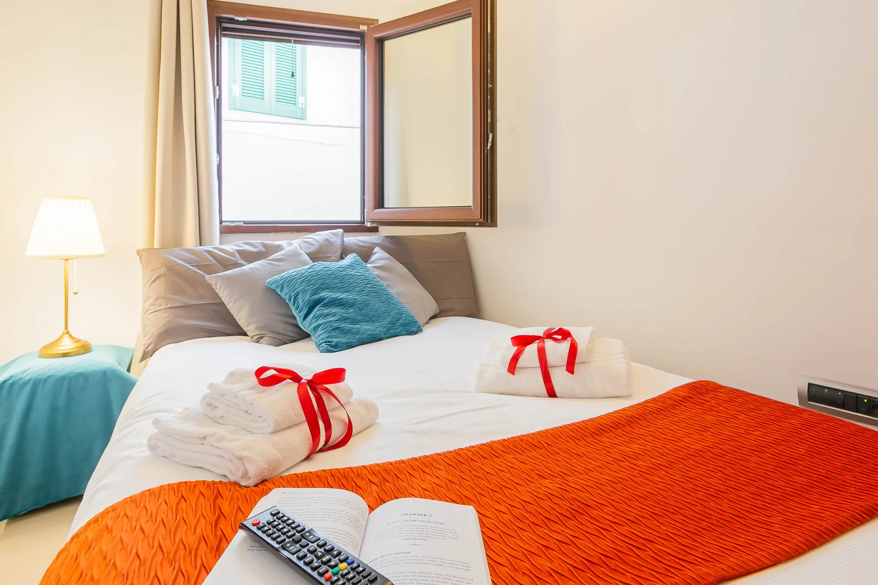 A bedroom with a neatly made bed, folded towels, and an open window.