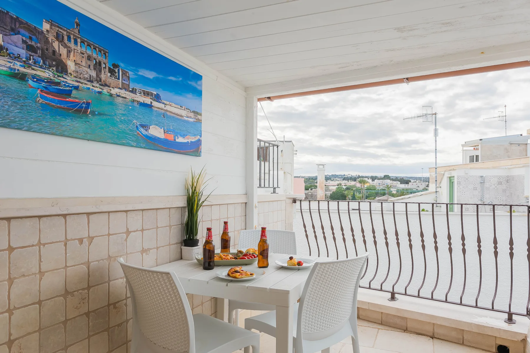 A covered terrace has a dining table and chairs beside an open railing.