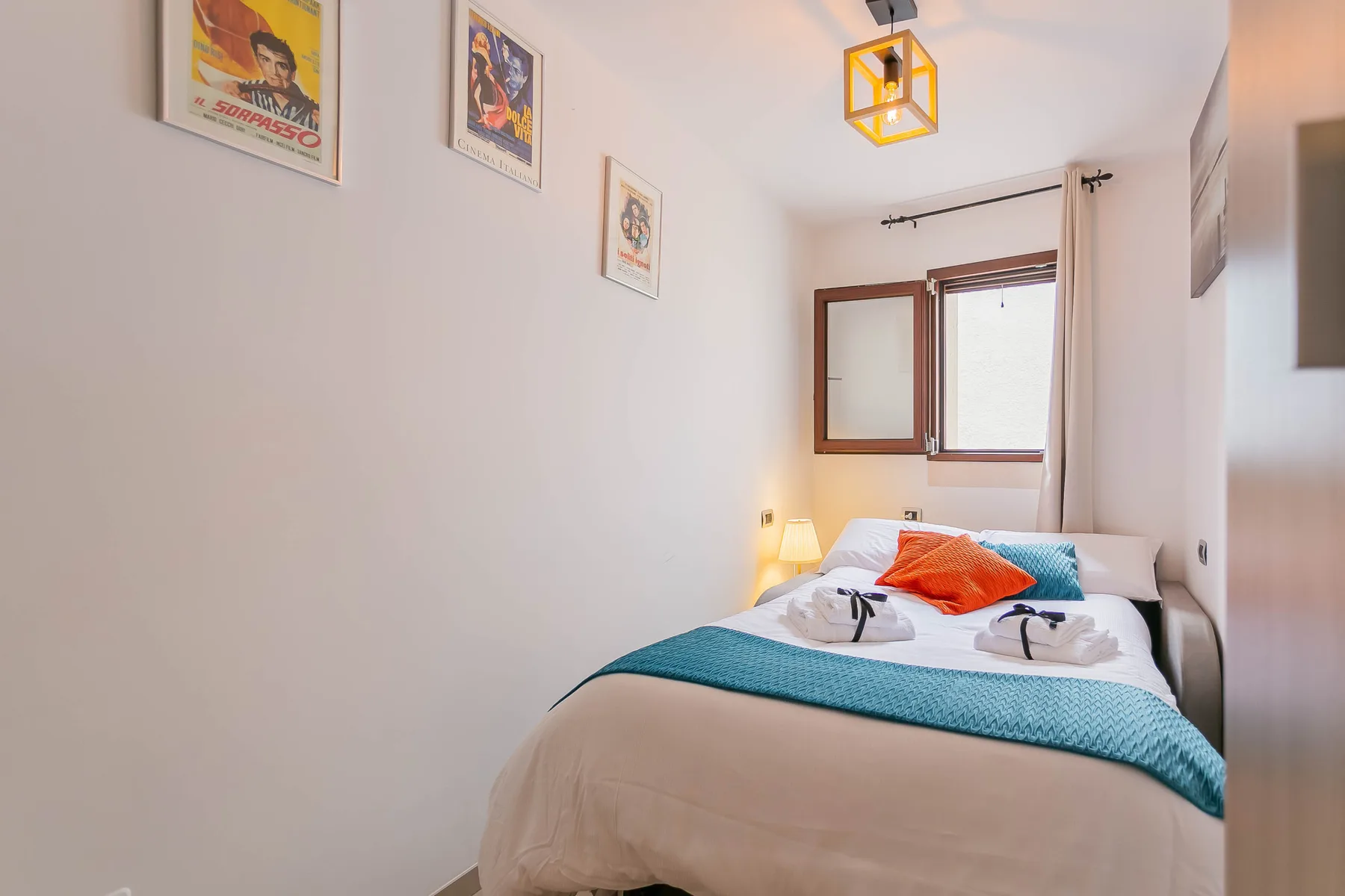 A bedroom with a neatly made bed, colorful pillows, and framed prints.