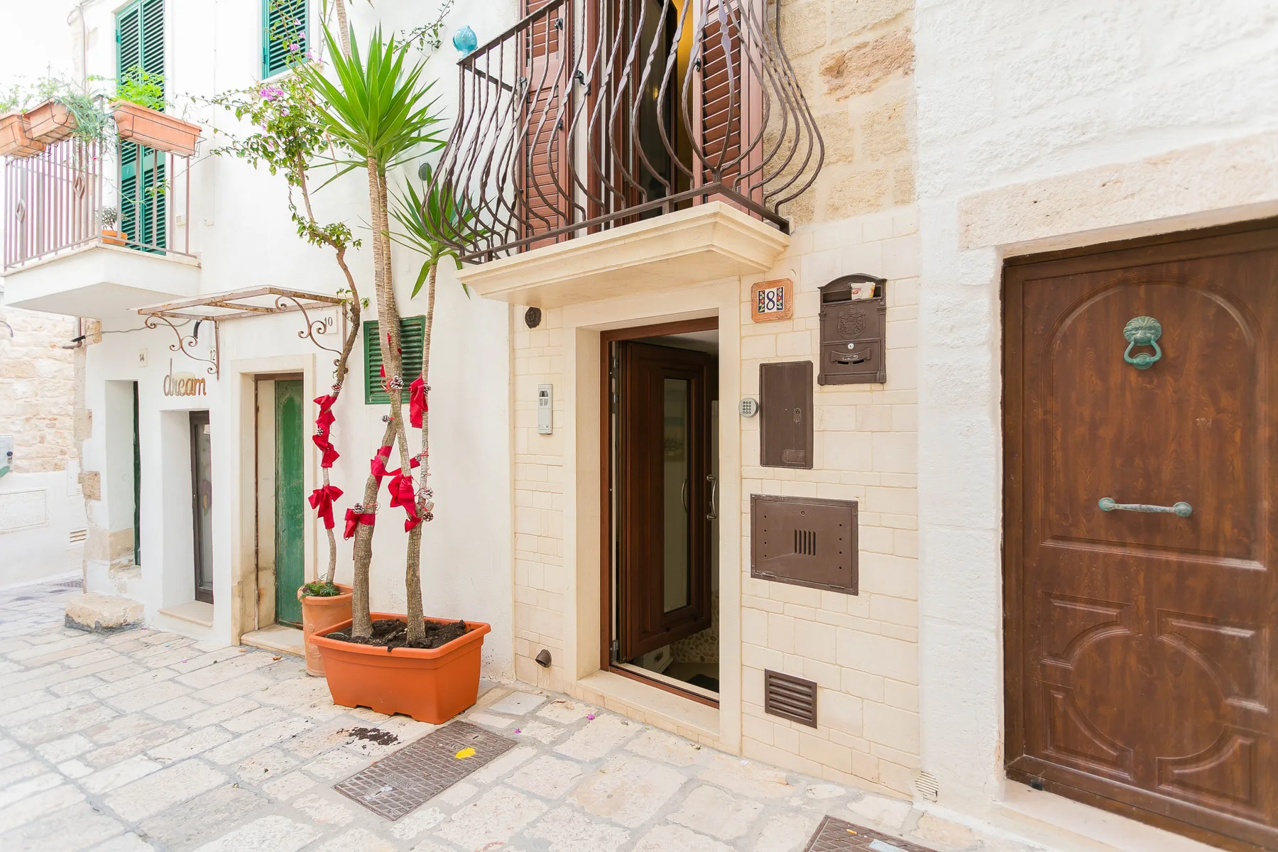 A light stone building entrance opens onto a paved walkway, with potted plants nearby.