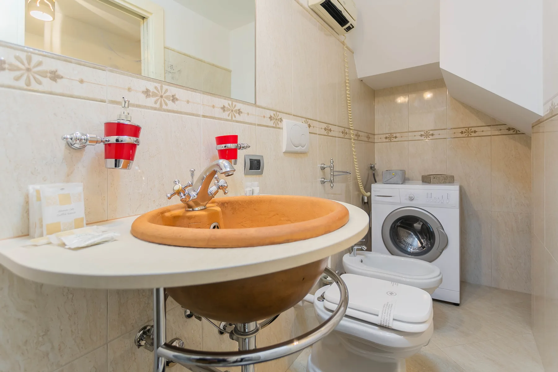 A tiled bathroom with a round basin, washing machine, and toilet.