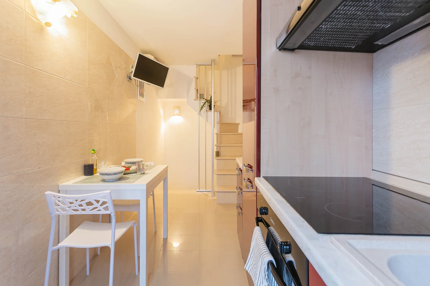 A compact kitchen with a dining table and a staircase in the background.