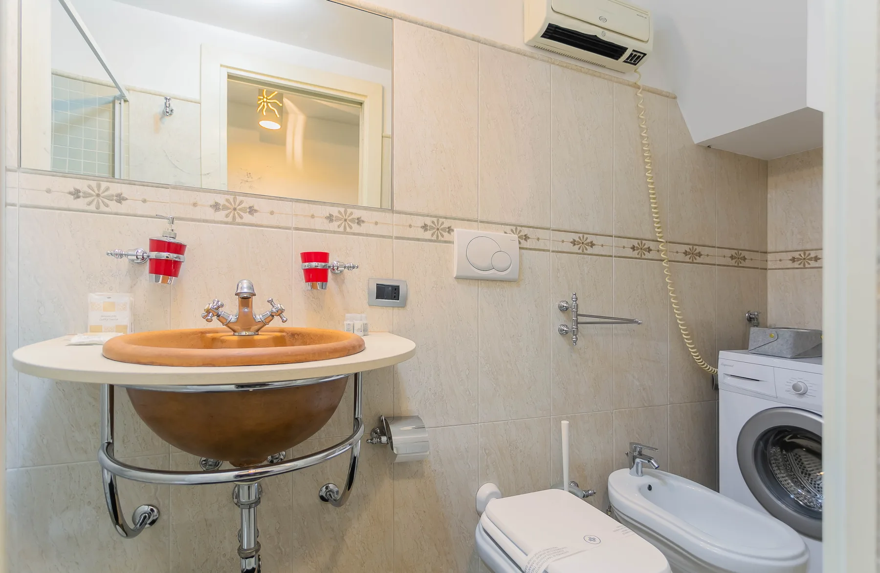 A tiled bathroom with a basin, toilet, bidet, and washing machine.