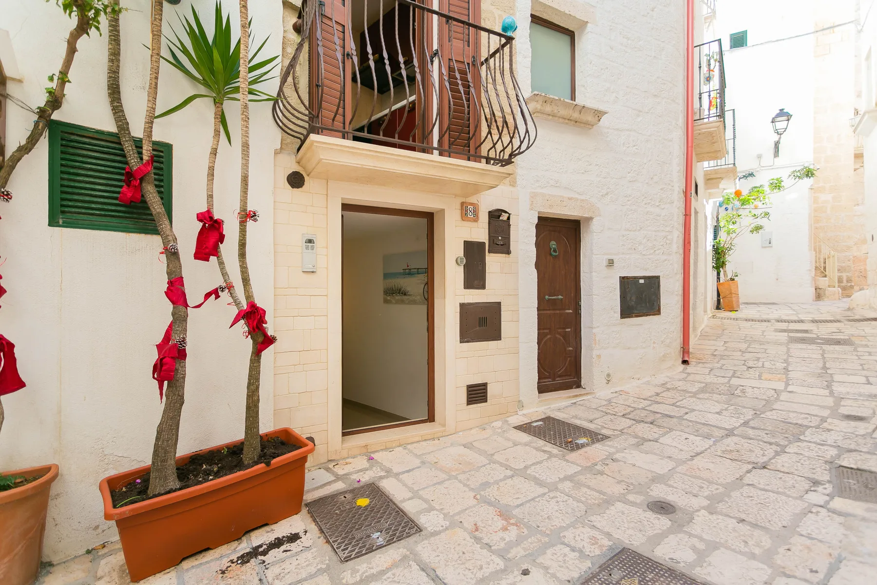 A stone-paved courtyard beside a light-colored building with a balcony and potted plants.