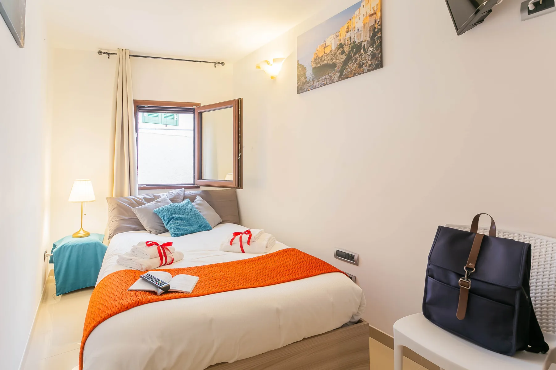A bedroom with a neatly made bed, colorful cushions, and a bedside lamp.