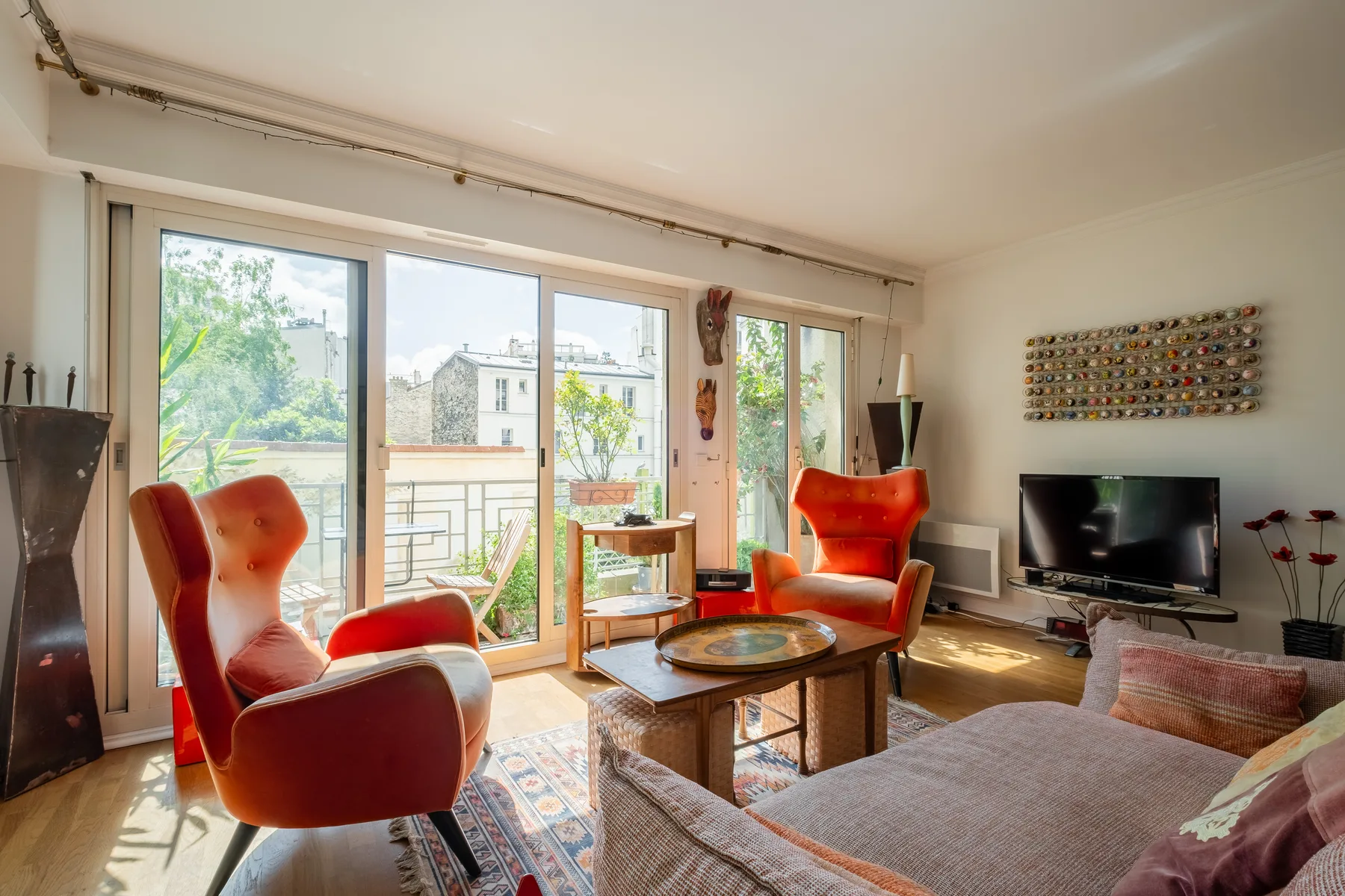 A bright living room with orange seating beside large windows overlooking a balcony.