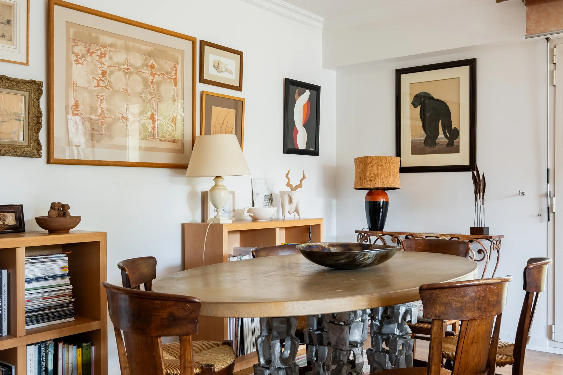 Comedor con una mesa de madera, sillas y obras enmarcadas en las paredes.