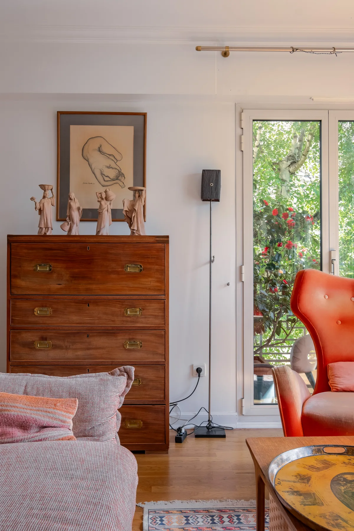 A bedroom with a wooden dresser, framed artwork, and a glass door overlooking greenery.