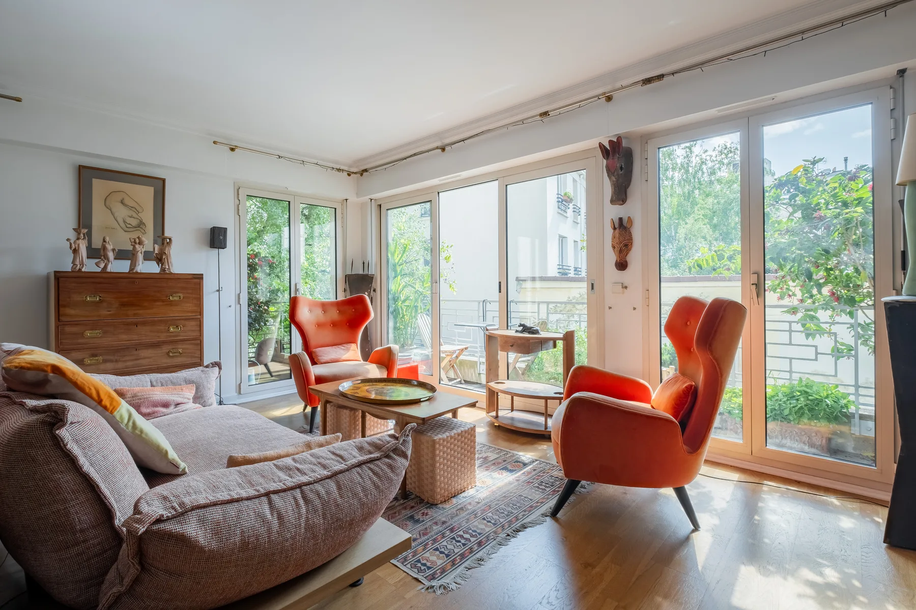 Una sala luminosa con asientos naranjas y grandes ventanas con vistas a la vegetación.