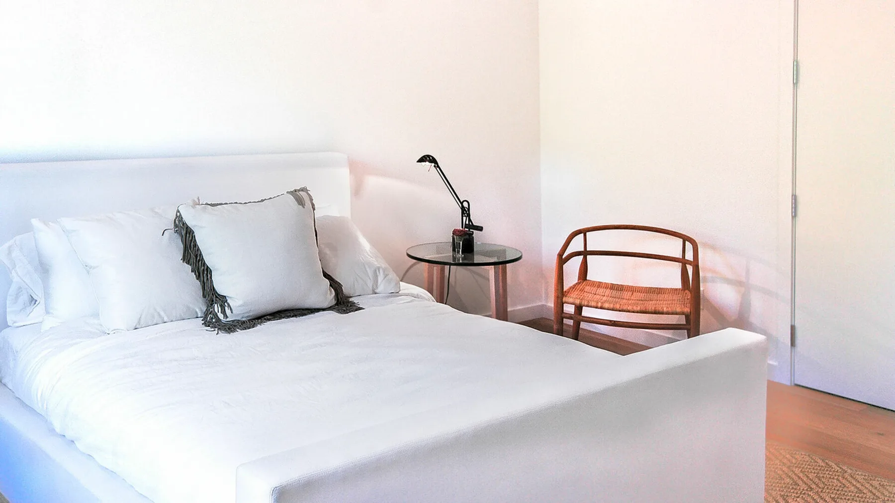 Un dormitorio luminoso con ropa de cama blanca y una mesa pequeña junto a la cama.
