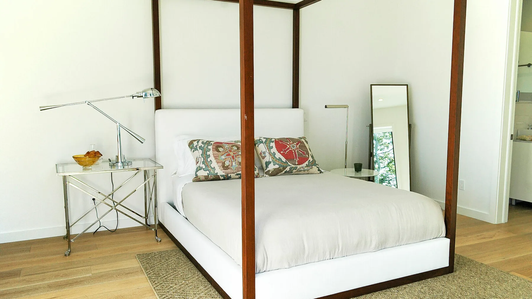 Un dormitorio con una cama blanca, almohadas estampadas y un espejo de pie.